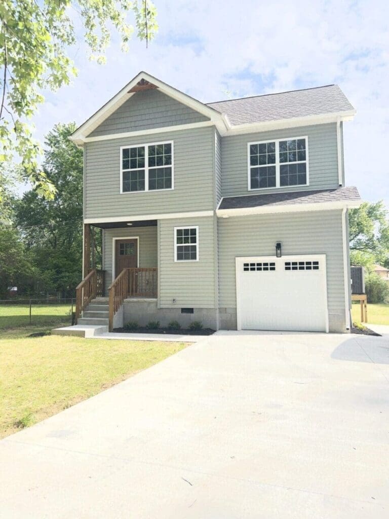 New two-story house with a front-facing garage and wooden front steps on a sunny day.