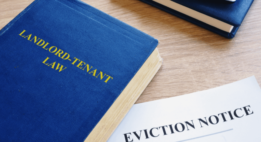 A blue book titled "Landlord-Tenant Law" and a paper labeled "Eviction Notice" are on a wooden surface next to another closed blue book.