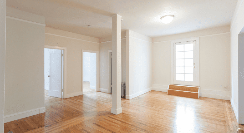 Empty room with light wood flooring, white walls, a ceiling light, and a door with glass panels leading outside. Two open doorways connect to adjoining rooms. Average Rent in Woodland Estates, Clarksville, TN.