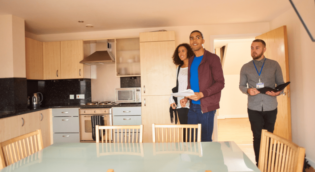 Three people stand in a modern kitchen with wooden cabinets and a glass dining table, holding documents. Rent in West Creek, Clarksville