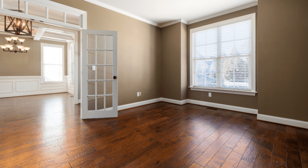 An empty room with wooden floors, beige walls, a window with blinds, a French door leading to another room, and a ceiling light fixture. average rent st bethlehem clarksville tn.