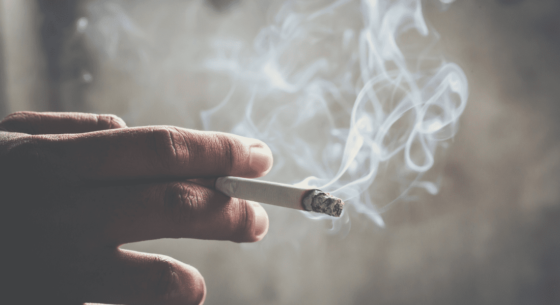 Hand holding a lit cigarette with smoke curling upwards against a blurred background. Can Tenant Smoke In Rented Property?