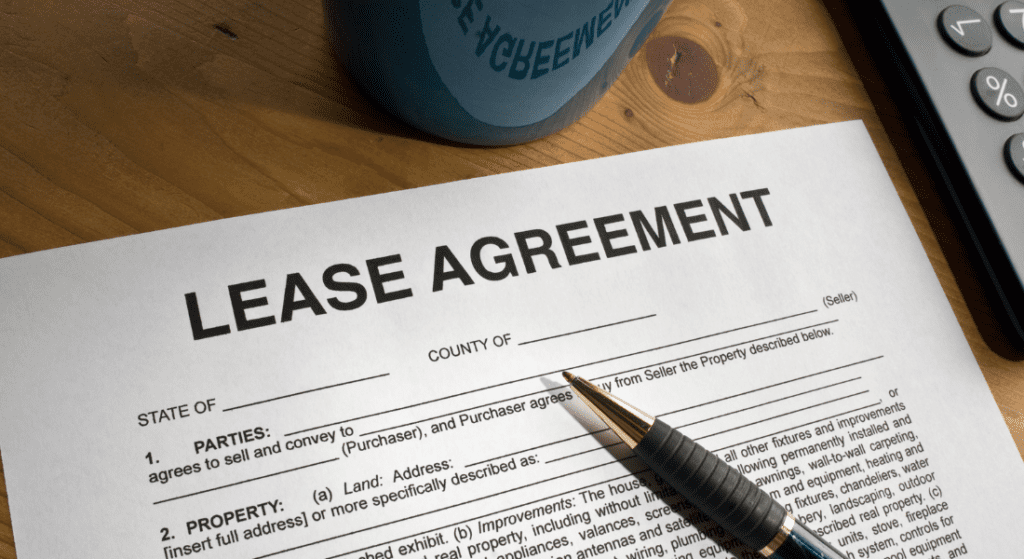 A lease agreement document is on a table next to a blue coffee cup and a calculator. A pen rests on the paper, ready for signing. Can Tenant Smoke In Rented Property?