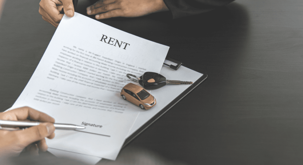 Two people discuss a rent agreement document on a clipboard with a pen, a toy car, and car keys on the table.