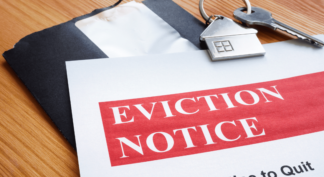 An eviction notice document on a wooden table, next to a black envelope and a key with a house-shaped keychain.