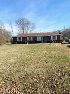 Single-story brick house with large front yard and clear blue sky in a suburban neighborhood