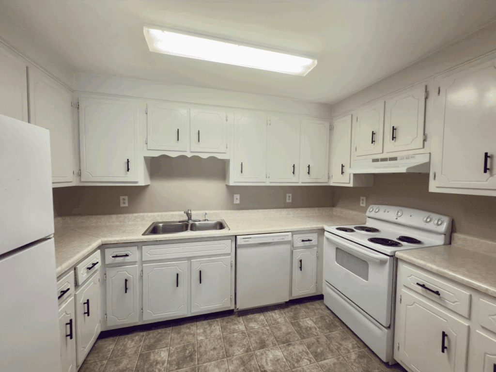 U-shaped kitchen with white cabinets, white appliances, a double sink, electric stove, dishwasher, and overhead fluorescent lighting.