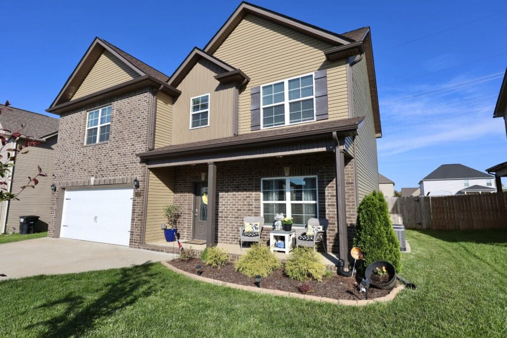Two-story suburban house with brick and siding exterior, attached two-car garage, and landscaped front yard on a sunny day.