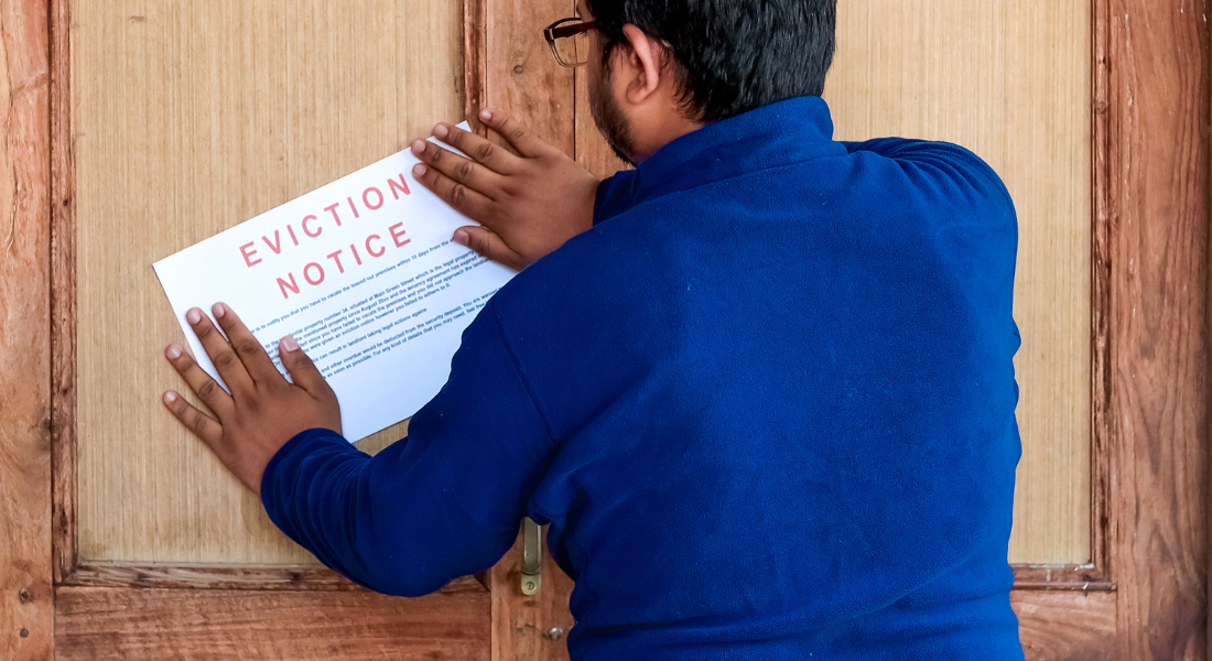 A person in a blue shirt posts an eviction notice on a wooden door.