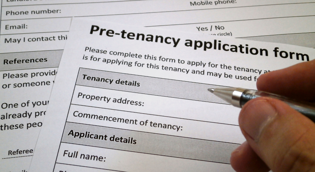 A hand holding a pen fills out a pre-tenancy application form that asks for tenancy and applicant details such as property address and full name.
