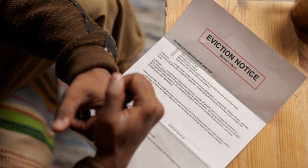 A person sits at a table looking at an eviction notice printed on white paper with bold red lettering at the top.