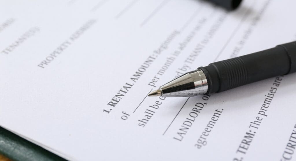A close-up of a black pen resting on a rental agreement form, with fields for rental amount and landlord information visible.