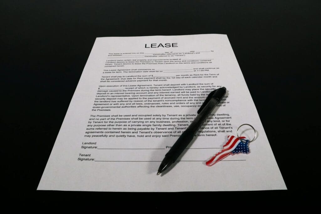 A lease agreement form on a black surface with a black pen and a keychain featuring an American flag.