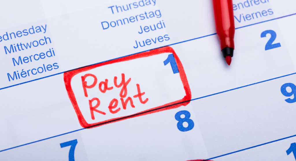 A calendar page with "Pay Rent" written in red marker and circled on the first day of the month; a red marker is nearby.