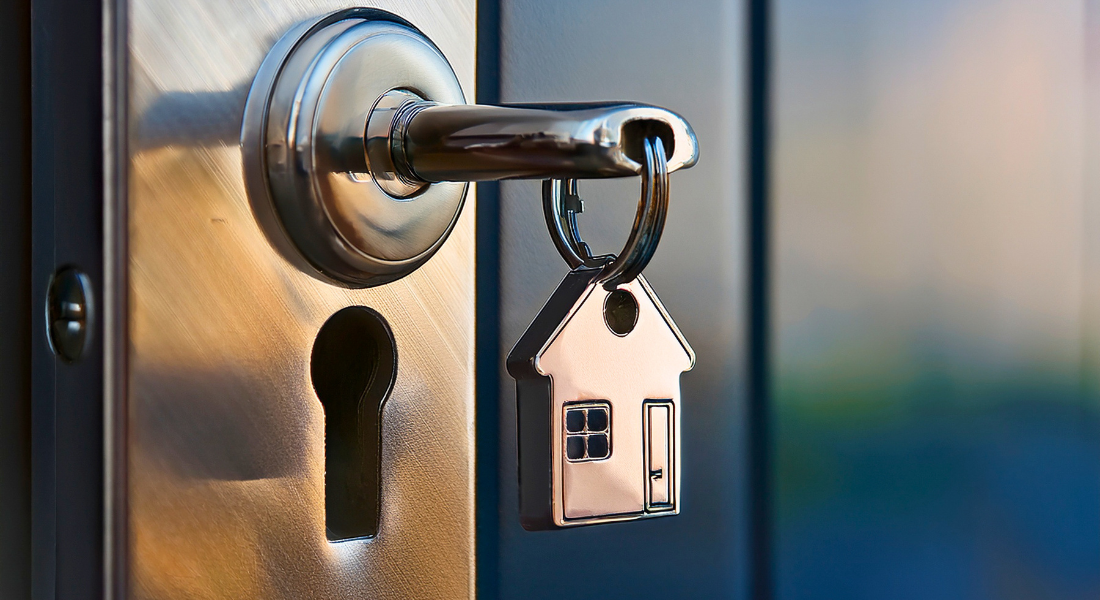 A key with a house-shaped keychain is inserted into a door lock on a metal door.
