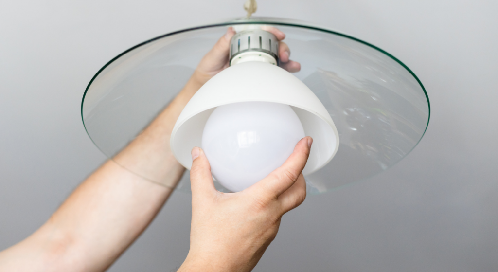 Person installing a round white light bulb into a ceiling light fixture with a glass cover.