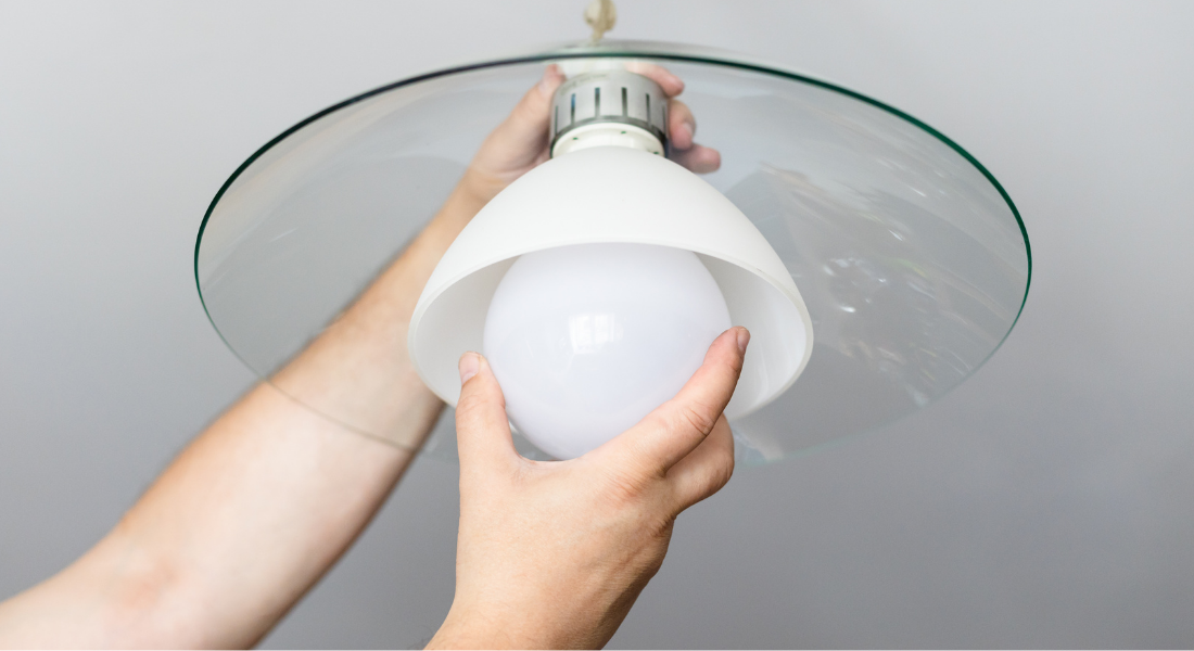 Person installing a round white light bulb into a ceiling light fixture with a glass cover.